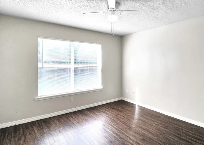 Bright and airy room with modern ceiling fan, large window, and elegant hardwood flooring.