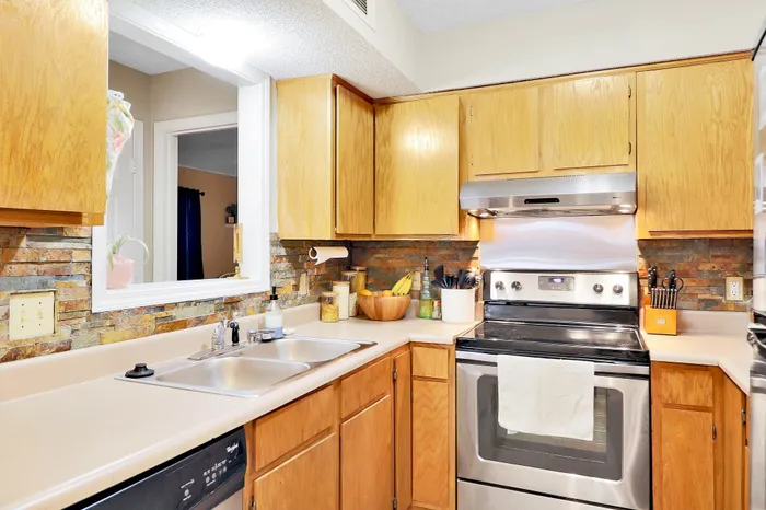 Charming kitchen with warm wood cabinetry, modern stainless steel appliances, and a stylish stone backsplash, offering a welcoming and functional space for cooking.