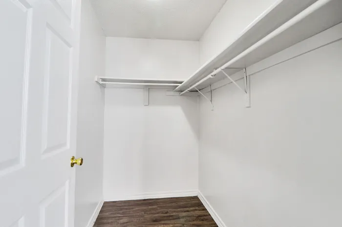 Spacious walk-in closet with sleek shelving and smooth hardwood flooring, perfect for organized storage and style.