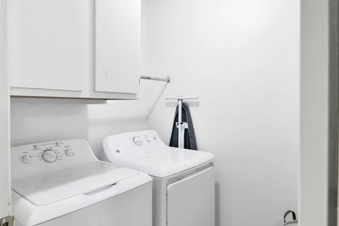 Chic laundry room with top-loading washer and dryer, featuring sleek white cabinetry and ample storage space.