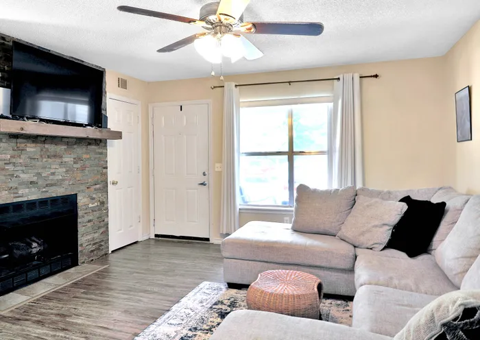 Inviting living room with a cozy L-shaped sofa, sleek ceiling fan, and elegant stone fireplace, perfect for relaxation and comfort.