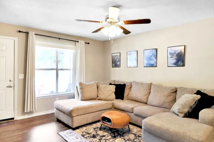 Inviting living room showcasing a cozy beige sectional sofa, stylish ceiling fan, and elegant wall art, perfect for relaxing and entertaining.