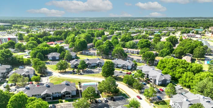 Aerial view of a picturesque residential complex surrounded by lush greenery, showcasing modern apartments and a peaceful suburban neighborhood under a bright blue sky.