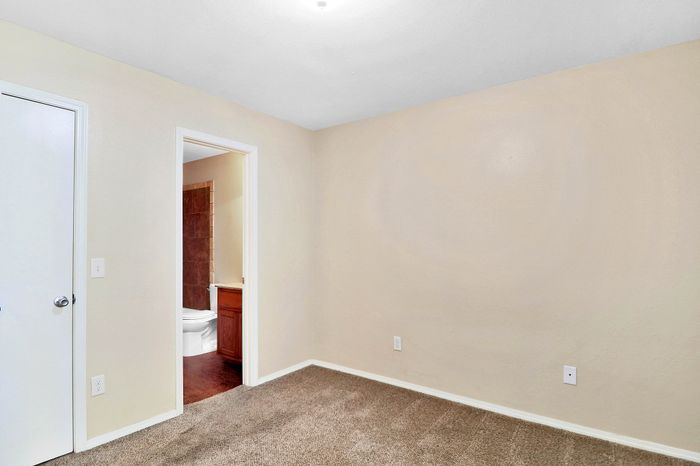 Bright and cozy room with plush carpet and neutral walls, featuring a modern bathroom with elegant wooden accents.