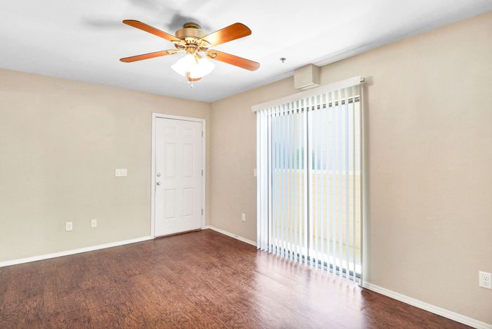 Bright and inviting living room with elegant hardwood floors, ceiling fan, and sliding glass door to a private balcony.
