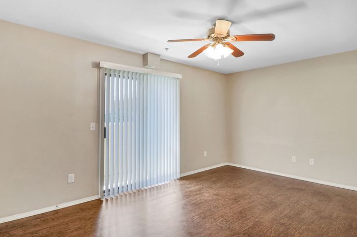Bright and airy room with sleek wood floors, large window, and modern ceiling fan, ideal for comfortable living.