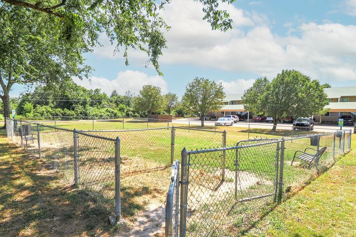 Charming outdoor pet-friendly area with lush greenery, secure fencing, and convenient parking at modern apartment complex.
