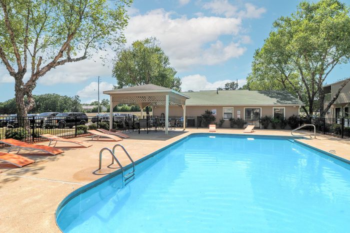 Inviting outdoor swimming pool area with sun loungers and a charming covered seating space surrounded by lush greenery.