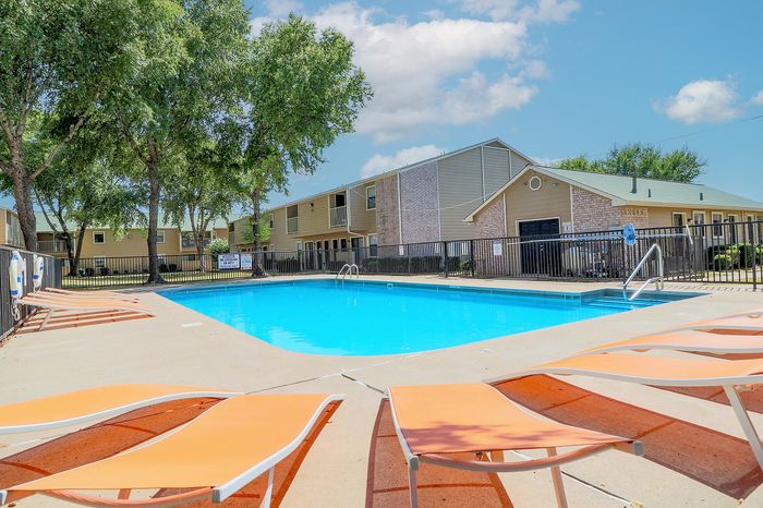 Inviting apartment complex pool area with vibrant orange loungers and lush greenery, perfect for relaxing under the sun.