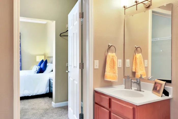 Inviting apartment interior showcasing a cozy bathroom with modern fixtures, leading to a bright bedroom adorned with plush blue accents.