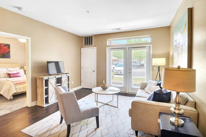 Inviting living room with elegant decor, cozy seating arrangement, and natural light streaming through glass doors, leading to a charming bedroom.