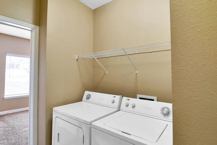 Convenient laundry nook with modern washer and dryer, beige walls, and a practical storage shelf.