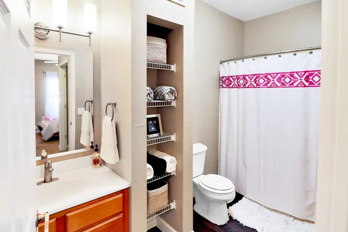 Bright and inviting bathroom with modern fixtures, elegant shelving, and a chic shower curtain accented with bold pink patterns.