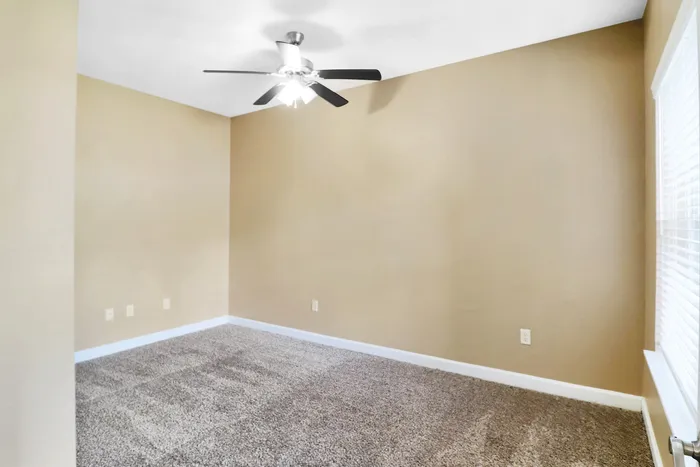 Bright, cozy room with plush carpet and a modern ceiling fan, perfect for a serene living space.