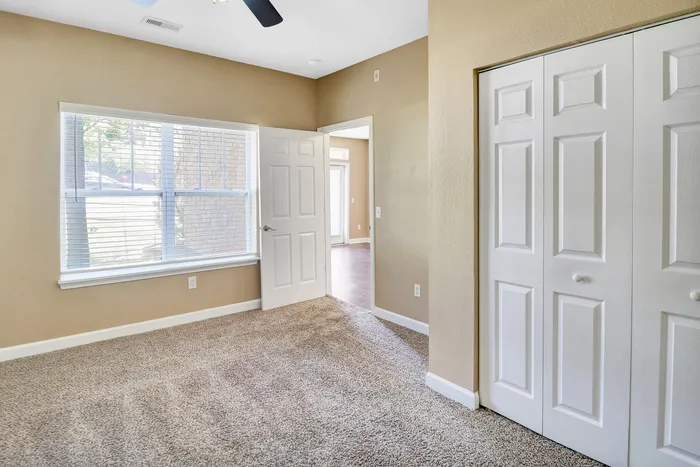 Bright and cozy bedroom with plush carpeting, double closet doors, and a large window offering ample natural light.
