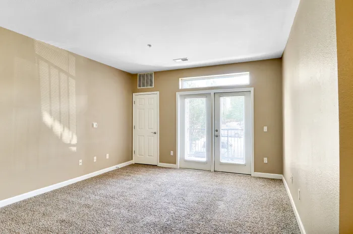 Bright and inviting room with plush carpeting, beige walls, and elegant French doors leading to a balcony.