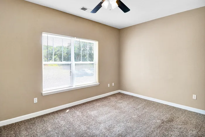 Bright and inviting room with plush carpeting and large window, perfect for a cozy and modern living space.