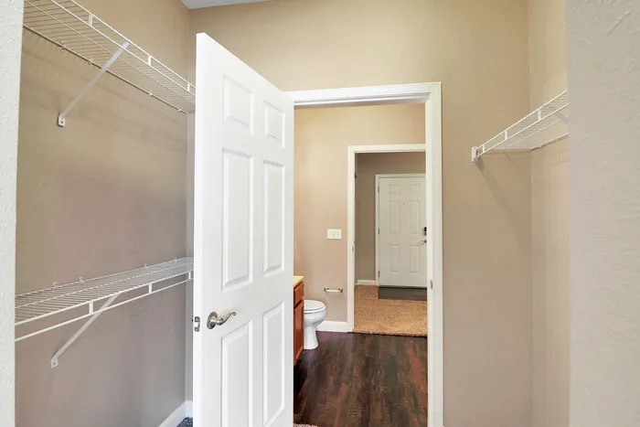 Inviting walk-in closet with ample shelving, opening to elegant bathroom with dark wood floors and neutral walls.