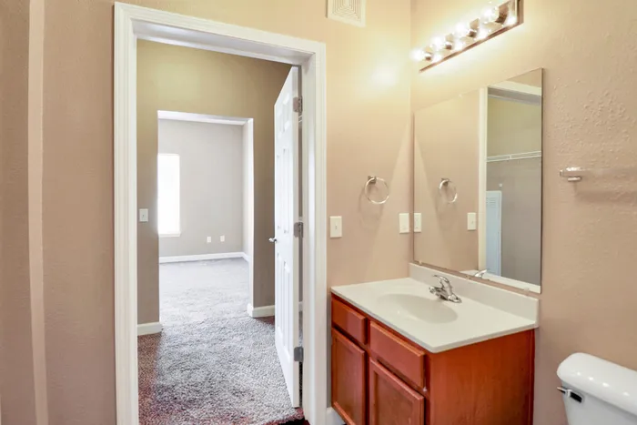 Bright and inviting bathroom with elegant lighting, spacious vanity, and view into a cozy carpeted bedroom.
