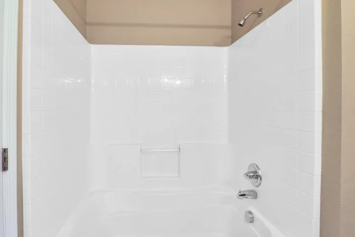 Pristine white tiled bathtub and shower area with sleek modern fixtures and a convenient wall shelf.