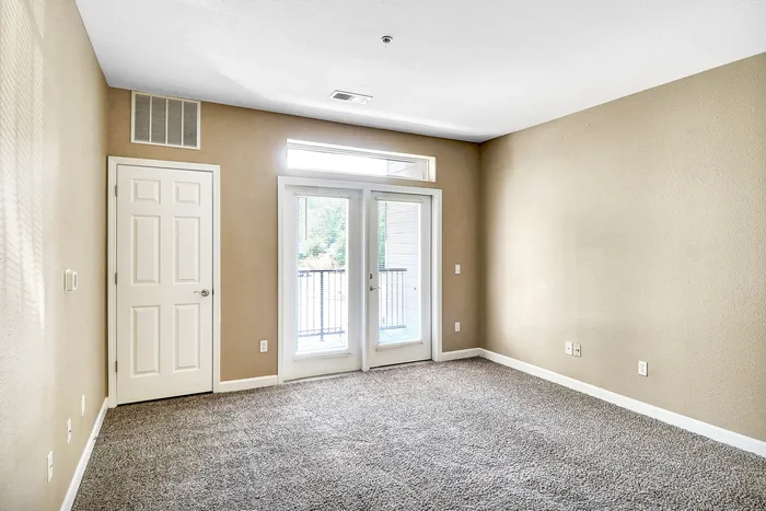 Bright and spacious bedroom with soft carpeting, elegant French doors, and abundant natural light.