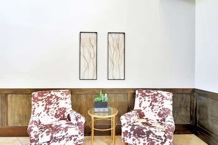 Elegant seating area with two cow-print armchairs, a modern glass-top table, and minimalist wall art creating a chic and inviting space.