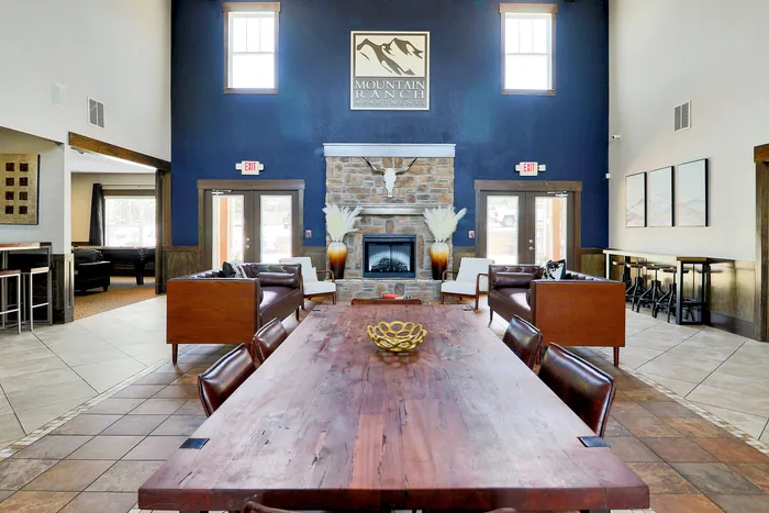 Elegant apartment lobby featuring a cozy stone fireplace, plush leather seating, and rustic decor creating a warm, inviting atmosphere.