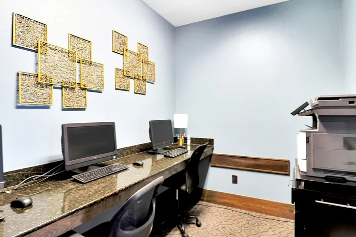 Modern business center featuring sleek computers, a multifunction printer, and chic gold wall art in a bright, professional setting.