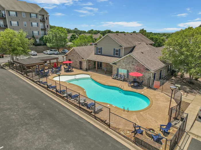Inviting outdoor pool at a modern apartment complex, surrounded by loungers and vibrant red umbrellas, perfect for relaxation and leisure.