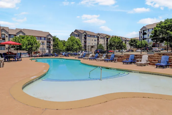 Inviting community pool with lounge chairs and umbrellas, surrounded by modern apartment buildings under a clear blue sky.