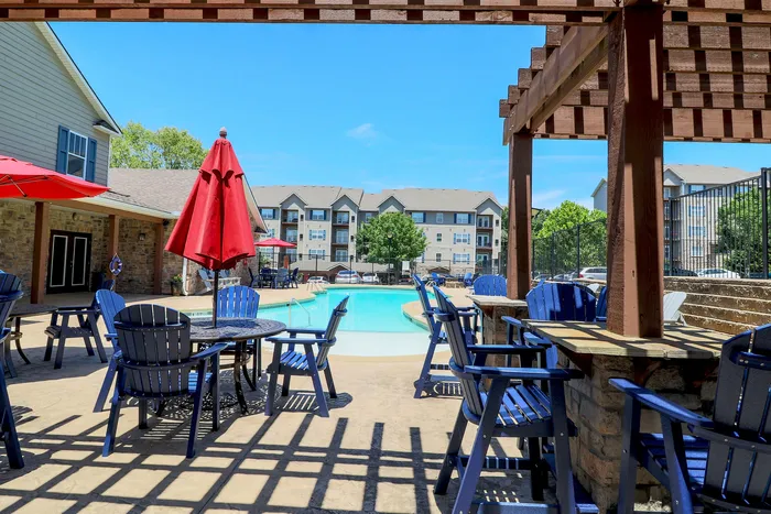 Inviting poolside lounge area with vibrant blue chairs and red umbrellas, perfect for relaxation in a charming apartment community.