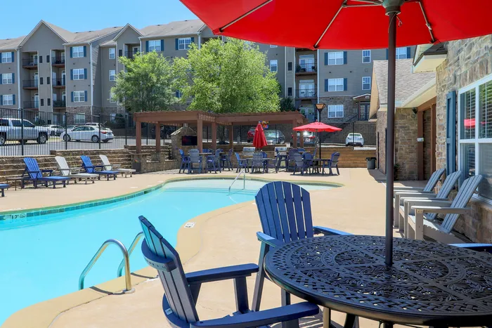 Inviting apartment complex with a sparkling pool, lounge chairs, and vibrant red umbrellas for a perfect outdoor relaxation experience.