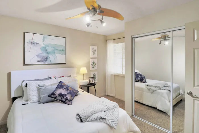 Chic bedroom with cozy bedding, mirrored sliding closet doors, and modern ceiling fan, exuding comfort and style.