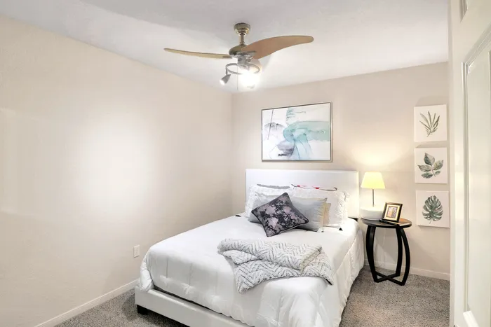 Cozy bedroom featuring a plush white bed, modern art, and a stylish ceiling fan, creating a serene retreat.
