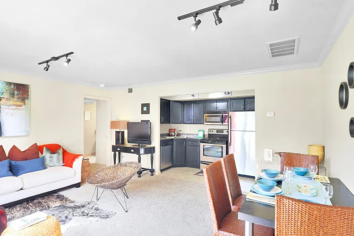 Bright and inviting open-concept living space featuring a cozy lounge area, modern kitchen with stainless steel appliances, and stylish dining table set for four.
