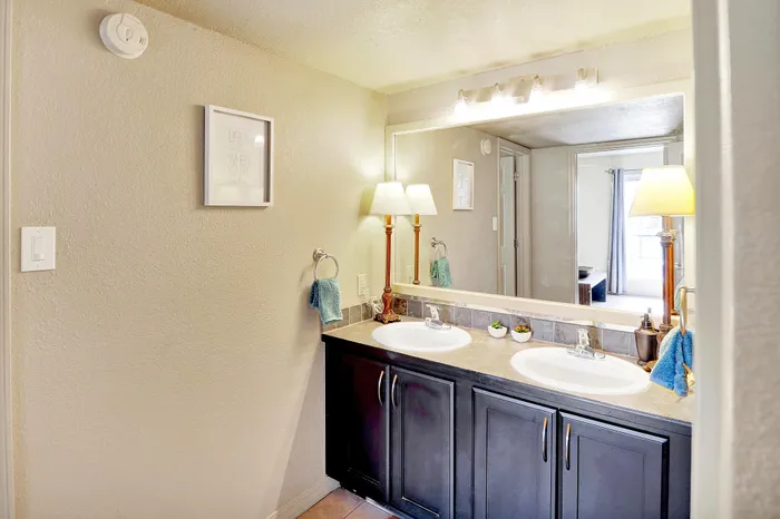 Bright and elegant bathroom featuring modern dual sinks, stylish lighting, and contemporary decor with warm, inviting tones.