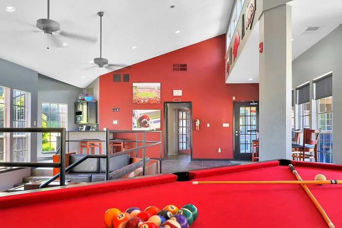 Vibrant lounge area featuring a pool table, comfortable seating, high ceilings, and abundant natural light, perfect for social gatherings.