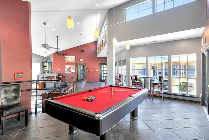 Bright and inviting recreational room with a sleek red felt pool table, modern seating, and expansive windows providing ample natural light.