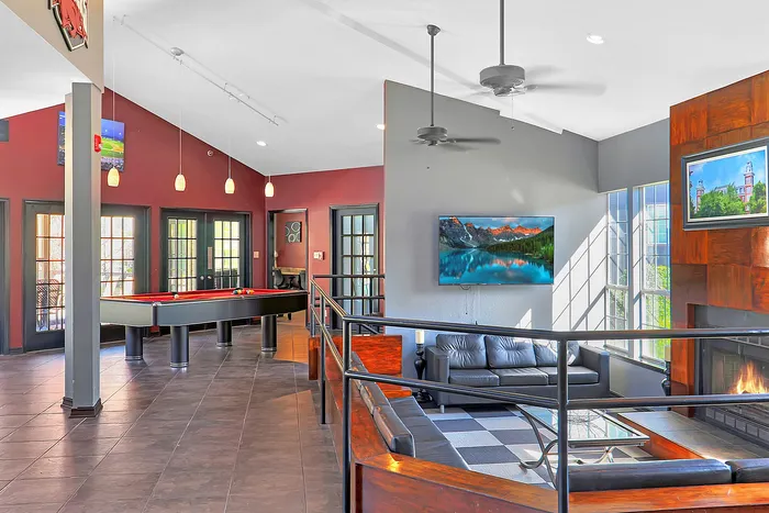 Lively recreation room featuring a billiards table, contemporary seating area, cozy fireplace, and natural light streaming through large windows.