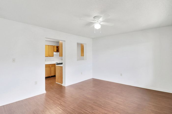 Bright open living area with sleek hardwood floors leading to a cozy kitchen featuring warm wooden cabinetry.