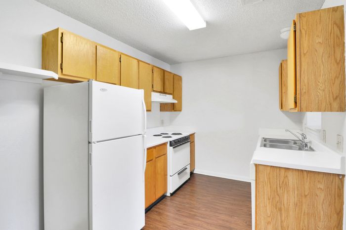 Bright kitchen with sleek white appliances, warm wooden cabinets, and polished flooring.