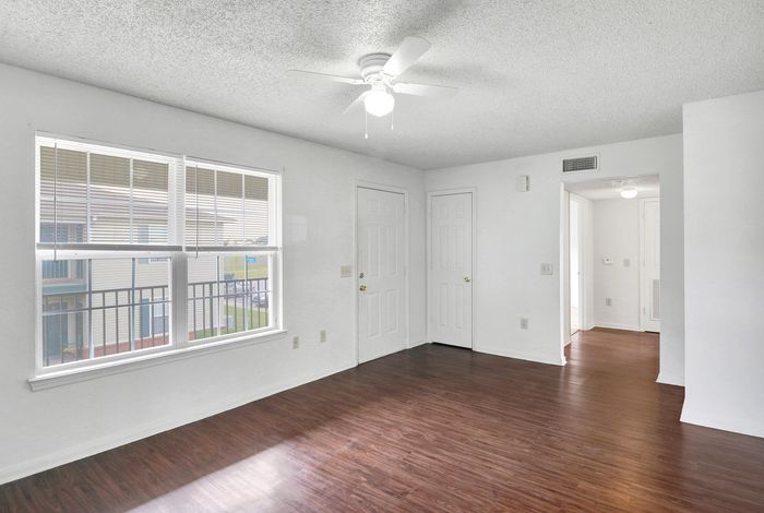 Bright apartment interior with gleaming wood floors, large window with blinds, and fresh white walls.
