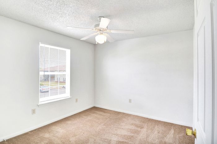 Bright and airy bedroom with soft carpet flooring, large window, and elegant ceiling fan.