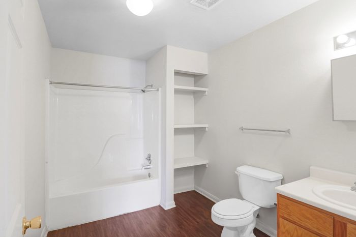 Modern bathroom with sleek white bathtub, elegant wooden flooring, and practical shelving for storage.