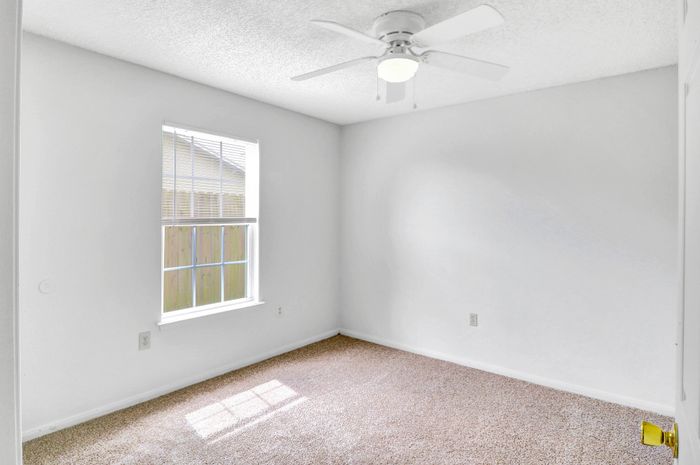 Bright and airy bedroom with plush carpeting and a large sunlit window, ideal for cozy living.