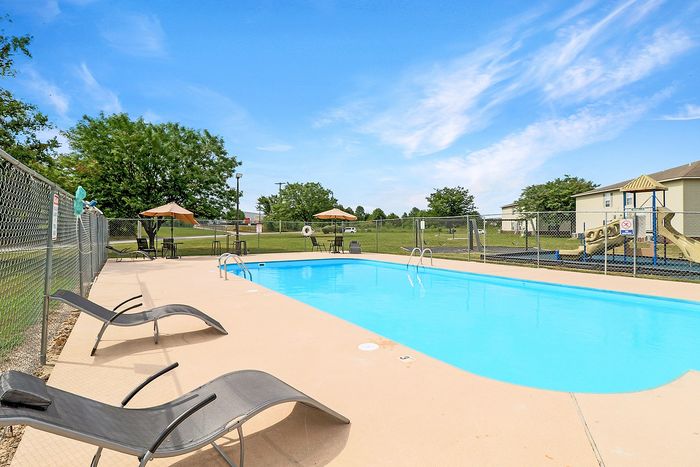 Inviting outdoor pool area with sleek lounge chairs and umbrellas, set against a lush green landscape and playground.