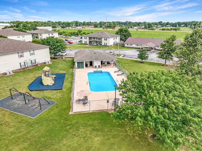Aerial view of a charming residential complex featuring a sparkling swimming pool, lush green lawns, and a playground area, perfect for family living.