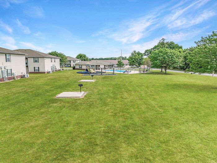 Expansive green space with modern apartment buildings, playground, and inviting pool under a clear blue sky.