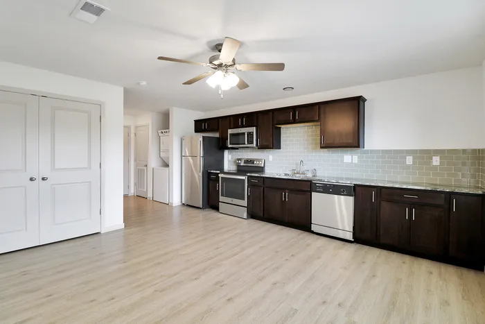 Modern open kitchen with stainless steel appliances, dark wood cabinets, and light wood flooring, offering a spacious and inviting atmosphere.