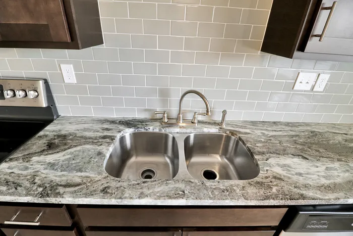 Modern kitchen featuring a sleek double sink with elegant marble countertops and stylish tile backsplash.